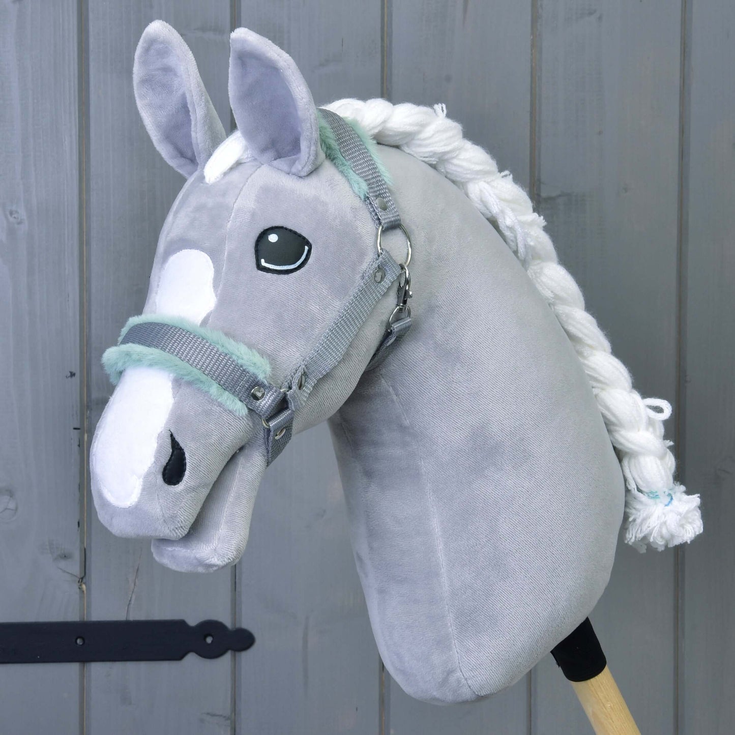 The Hobby Horse LarDen Halter grey with mint fur—a plush gray hobby horse accessory with a white mane and facial markings—set against a gray wooden background.