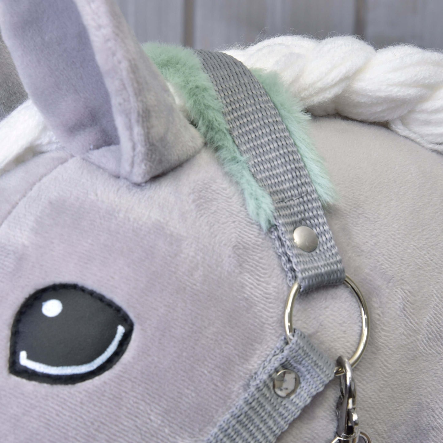 Close-up of a plush gray unicorn toy with a black and white embroidered eye, white yarn mane, mint-green accents, and the Hobby Horse LarDen "Halter grey with mint fur" featuring a silver ring and fastener.