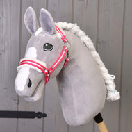 Hobby Horse LarDen „Halfter roter Streifen mit Fell“ auf einem grauen Hobby Horse aus Plüsch mit weißer Mähne und Halfter mit roten Streifen auf einem Holzstab vor einer grauen Holzwand.