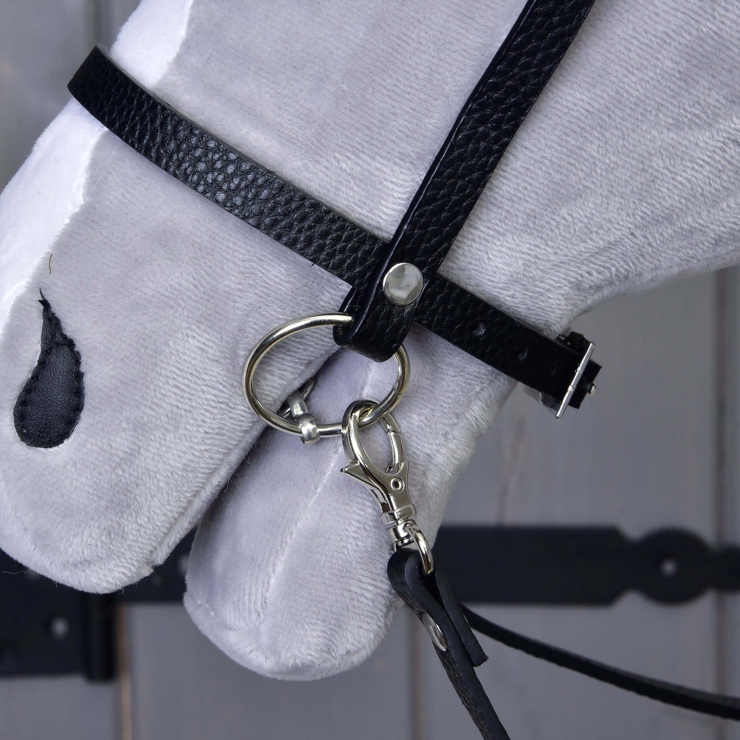 Nahaufnahme eines weißen Plüschpferdekopfes mit Komplettes Kunstlederzaumzeug mit Ziersteinen von Hobby Horse LarDen, mit abnehmbaren Zügeln und englischem Nasenriemen mit Metallgebiss, vor hölzernem Hintergrund mit sichtbaren dunklen Beschlägen.