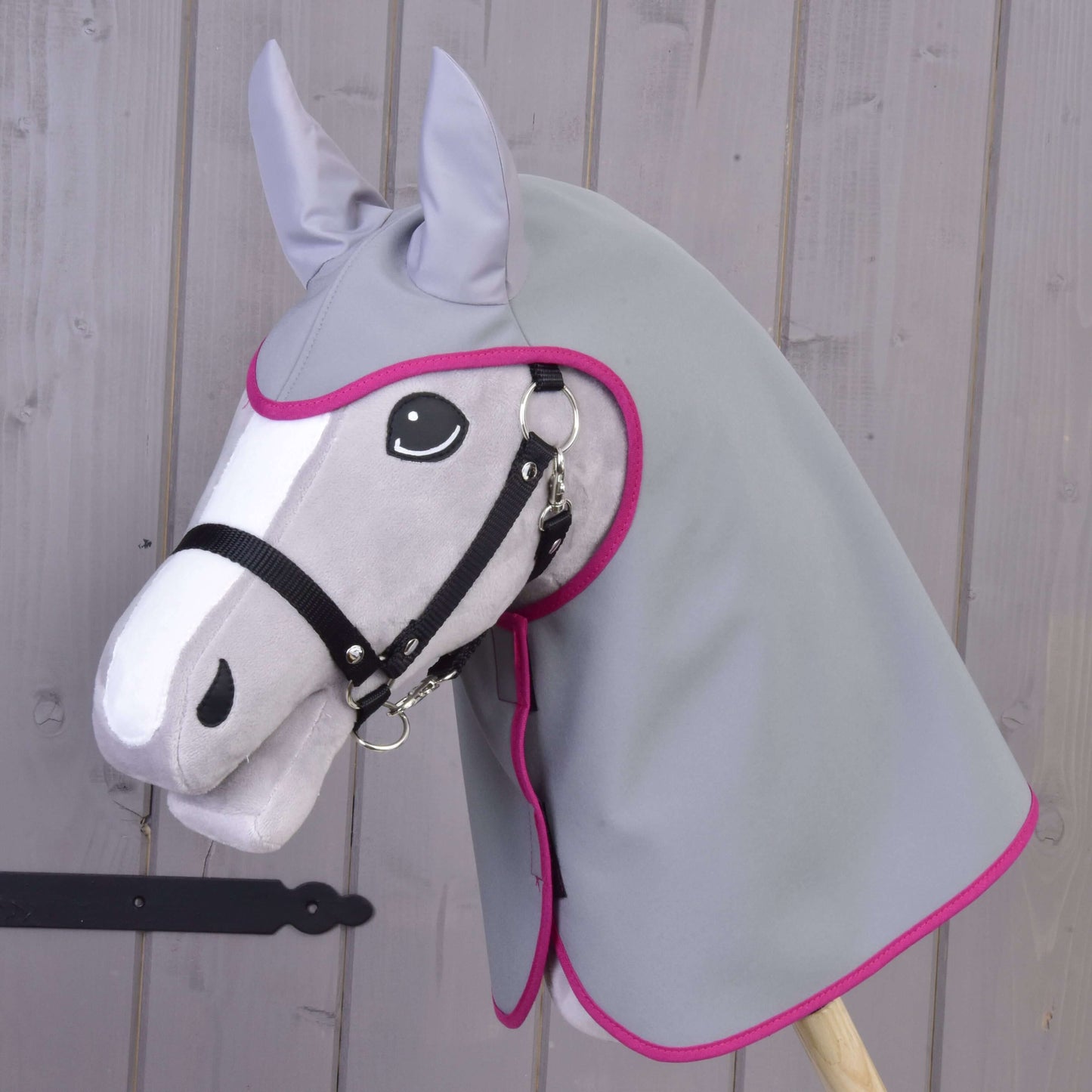 Imperméable gris de Hobby Horse LarDen sur un Hobby Horse gris en peluche avec capuche assortie en tissu à bordure rose et licol noir, présenté sur un fond en bois.