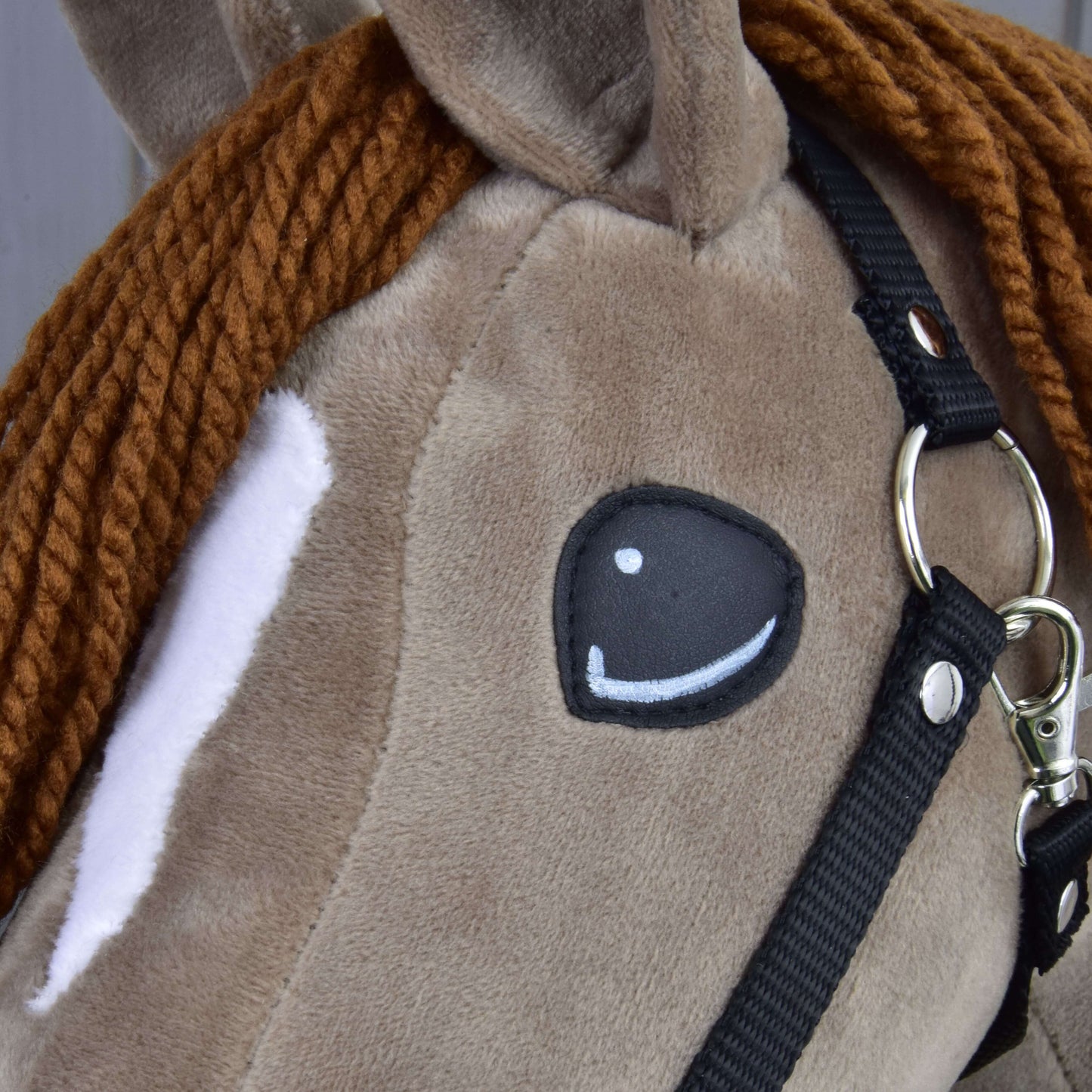 Gros plan sur le Hobby Horse Oliver de Hobby Horse LarDen avec licol noir, plus licol en fourrure offert, avec crinière tressée en fil brun, tache blanche autour de l’œil et œil cousu de style cartoon.