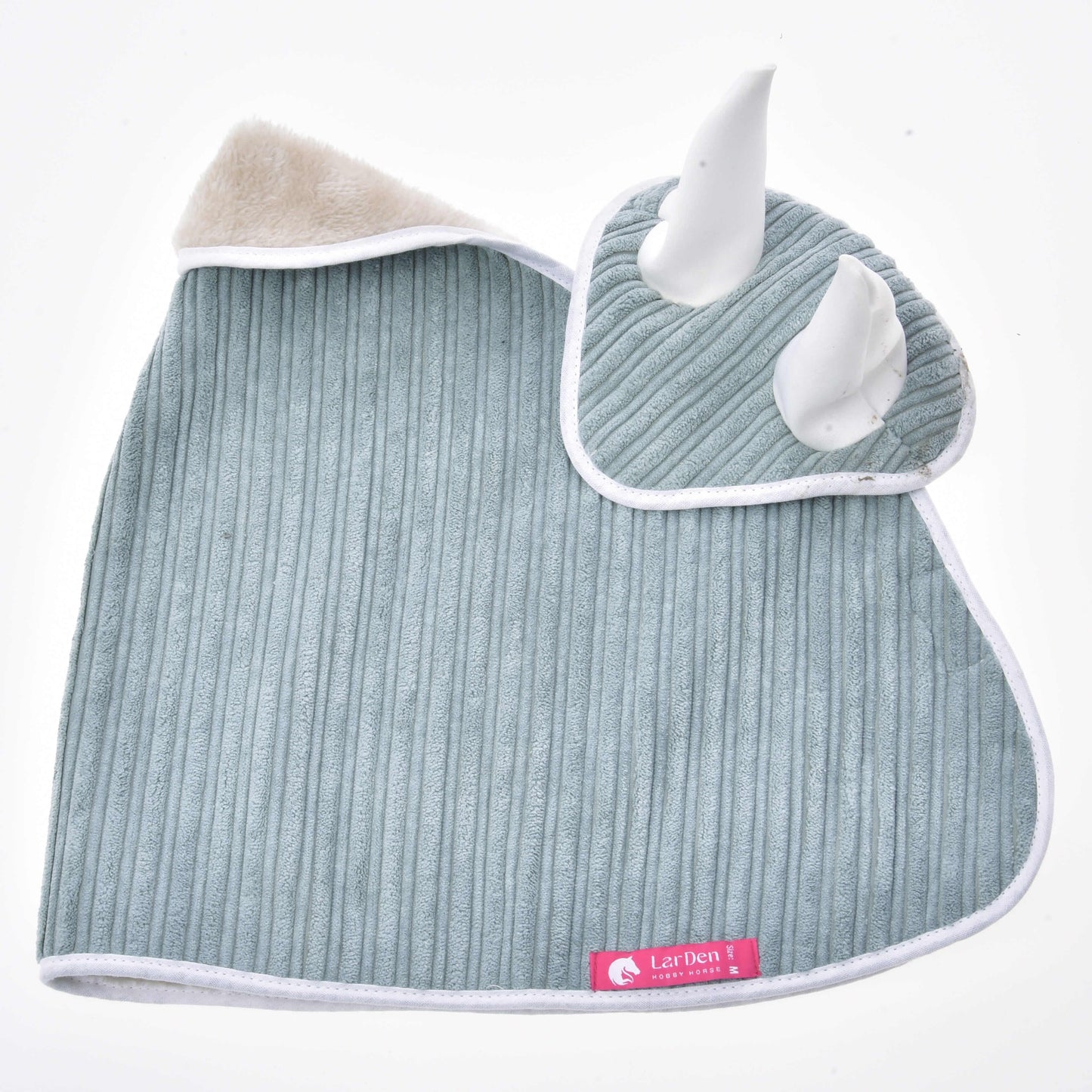 Ein weiches, geripptes, hellgraues Quadrat mit weißem Besatz aus dem Set Manchester Little Green von Hobby Horse LarDen mit zwei plüschigen weißen Hörnern, einer beigen flauschigen Ecke und einem rosa „Lazhen“-Label, flach liegend vor weißem Hintergrund.