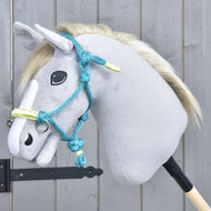 Hobby Horse LarDen Seilhalfter Türkis, gezeigt auf einem plüschigen Hobby Horse mit hellgrauem Kopf, weißer Mähne und blauer Trense, auf einem Holzstab vor einer grauen Holzwand.