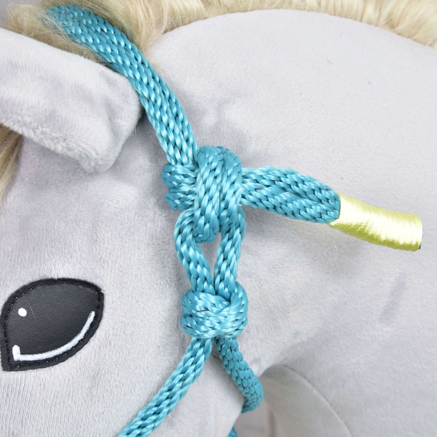 Gros plan sur le Licou en corde Turquoise de Hobby Horse LarDen sur une tête de Hobby Horse en peluche, avec oreille à extrémité jaune, œil noir cousu et crinière claire, un adorable accessoire pour tout passionné de Hobby Horse.