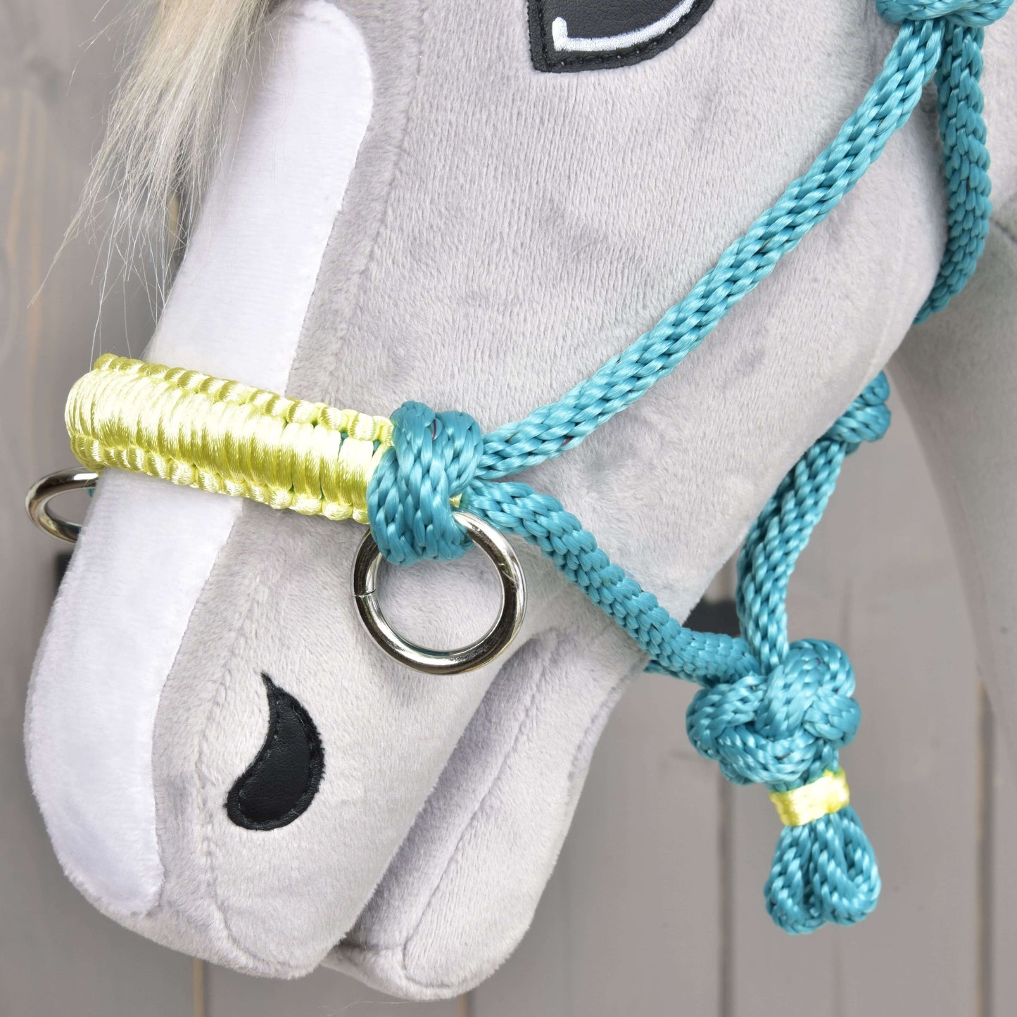 Gros plan sur un Hobby Horse en peluche gris de Hobby Horse LarDen, avec Licou en corde Turquoise et bride, yeux et naseaux noirs cousus, et crinière en fil blanc.