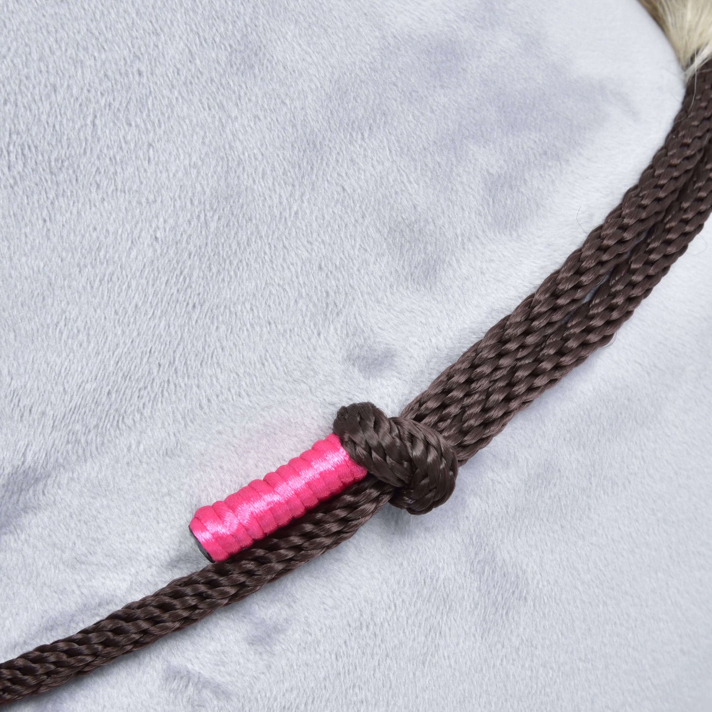Gros plan sur l’ensemble de corde Noir Cacao de Hobby Horse LarDen, un licol en corde marron tressée noué autour de l’encolure d’un cheval gris clair, avec une partie de la corde enveloppée d’un ruban rose vif.