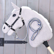 Hobby Horse LarDen „Hobby Horse - Führstrick Knitted Cremo-Blue“ in Grau mit schwarzem Zaumzeug und blau-weiß gestricktem Führstrick, hängt an einer Holzwand neben einem schwarzen Metallscharnier.