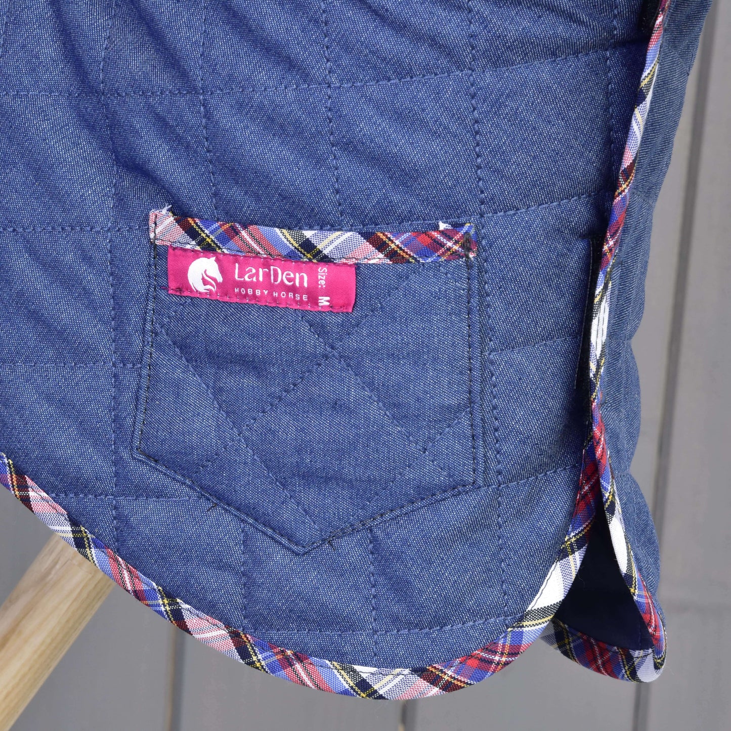 Ensemble Jean, couverture matelassée bleue de Hobby Horse LarDen, en gros plan, avec poche, bordure à carreaux multicolores et étiquette rose portant la mention Hobby Horse LarDen.