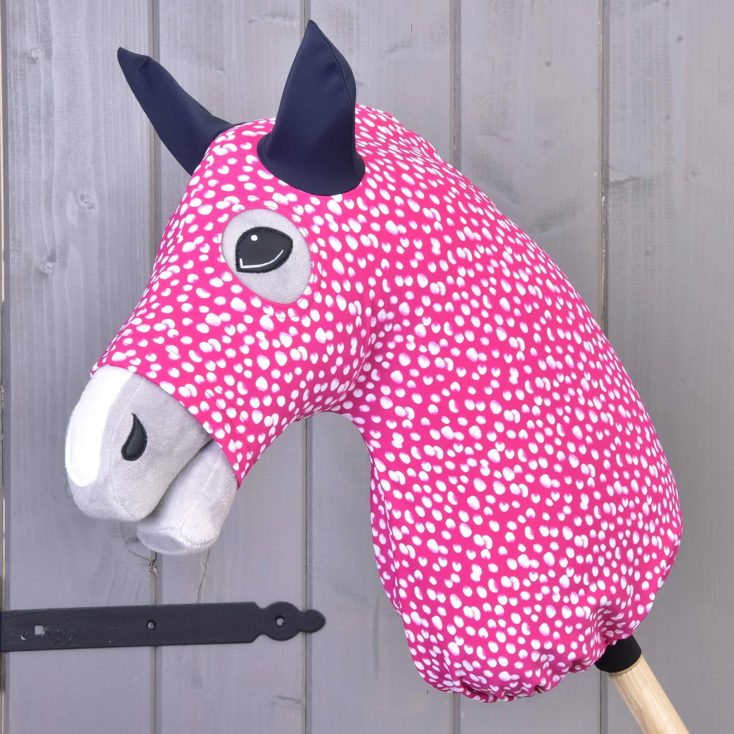 Combinaison de protection Hobby Horse Minie (Lycra) de Hobby Horse LarDen, Hobby Horse rose à taches blanches avec museau gris, oreilles noires, bâton en bois et housse lavable en Lycra pour un nettoyage facile.