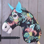 Combinaison de protection Hobby Horse Ananas (Lycra) de Hobby Horse LarDen, avec tête noire, motif vif d’ananas et de feuilles, oreilles bleues et museau blanc, montée sur un bâton en bois et présentée devant un mur en bois gris.