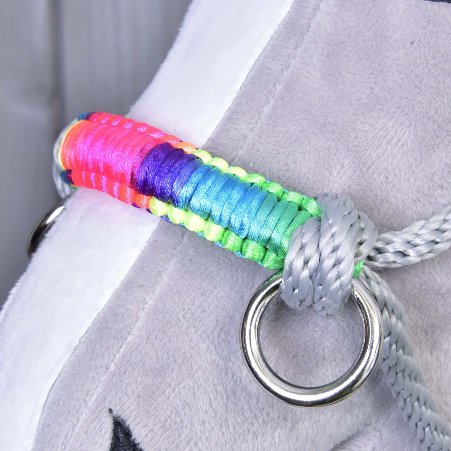 Licou en corde Manhattan de Hobby Horse LarDen, gros plan sur un objet en peluche gris avec une sangle arc-en-ciel sur un anneau métallique brillant, fixé par le licou, idéal comme accessoire unique pour votre Hobby Horse.