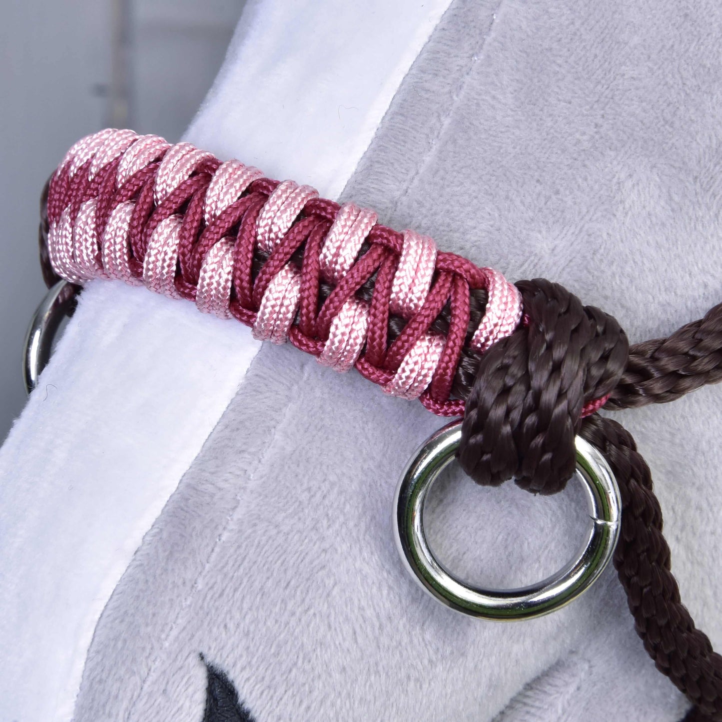 Licou en corde York de Hobby Horse LarDen, gros plan sur une bande tissée rose et rouge avec anneaux métalliques et corde marron, posée sur une surface grise douce, parfait comme accessoire élégant ou harnachement pour chevaux Hobby Horse ou en peluche.