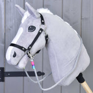 Rênes Manhattan de Hobby Horse LarDen sur un Hobby Horse gris avec crinière blanche, licol noir, rênes faites main et bâton en bois, présenté devant un mur en bois gris.
