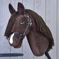 Hobby Horse Chianti mit Schwarzem Halfter von Hobby Horse LarDen, ein braunes Plüsch-Hobby Horse mit schwarzem Halfter, Knopfaugen, Garnmähne und weißem Nasenabzeichen, inspiriert von American Quarter Horses, vor einem hellgrauen Holz-Hintergrund.