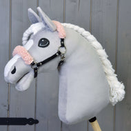 Ein plüschiges Hobby Horse LarDen mit grauem Gesicht, weißer Mähne und Schwarzes Halfter mit altrosa Fell - Kunstleder vor Holz-Hintergrund.