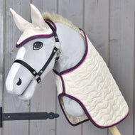 Set Supreme Crema von Hobby Horse LarDen mit einem Hobby Horse mit grauem Gesicht, weißer Schnauze und weißen Ohren, ausgestattet mit einer gesteppten cremefarbenen Decke und passender Fliegenhaube mit lila Einfassung, vor einer Holzwand.