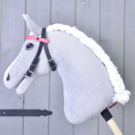 The Hobby Horse LarDen Bridle with 2 Headbands Pink (size M) features a gray hobby horse with a white yarn mane, black bridle (no noseband), and pink headband on a wooden stick, set against light gray wooden panels.