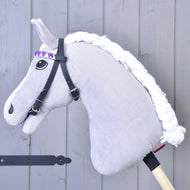 The Hobby Horse LarDen Bridle with 2 headbands purple (size M) features a gray plush horse with a white braided mane, black bridle without noseband, and a purple diamond-patterned ribbon on a wooden stick, set by a light gray wooden wall.