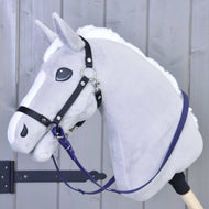 Nahaufnahme eines grauen Plüsch-Hobby Horse von Hobby Horse LarDen mit schwarzem Zaumzeug, weißer Mähne und Holzstab. Es trägt Gummierte Zügel - Dark purple und ist vor einem hellgrauen Holzhintergrund zu sehen.