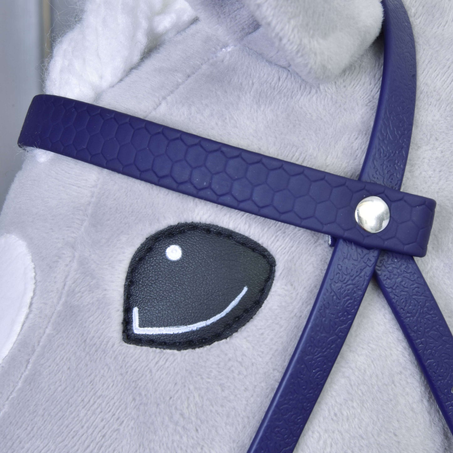Nahaufnahme eines Plüschpferdegesichts mit gesticktem schwarz-weißem Auge, das Hobby Horse LarDen Komplettes Zaumzeug mit Nasenriemen Dark Purple trägt; das Zaumzeug hat ein silbernes Knopfdetail und das Fell des Pferdes ist hellgrau.