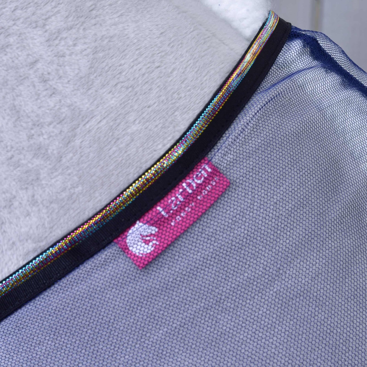 Gros plan de la Couverture anti-insectes LarDen de Hobby Horse LarDen, avec tissu en maille PES, bordure irisée et étiquette rose HARPER avec logo blanc. Le matériau blanc doux en arrière-plan met en valeur son design léger pour les accessoires de Hobby Horse.
