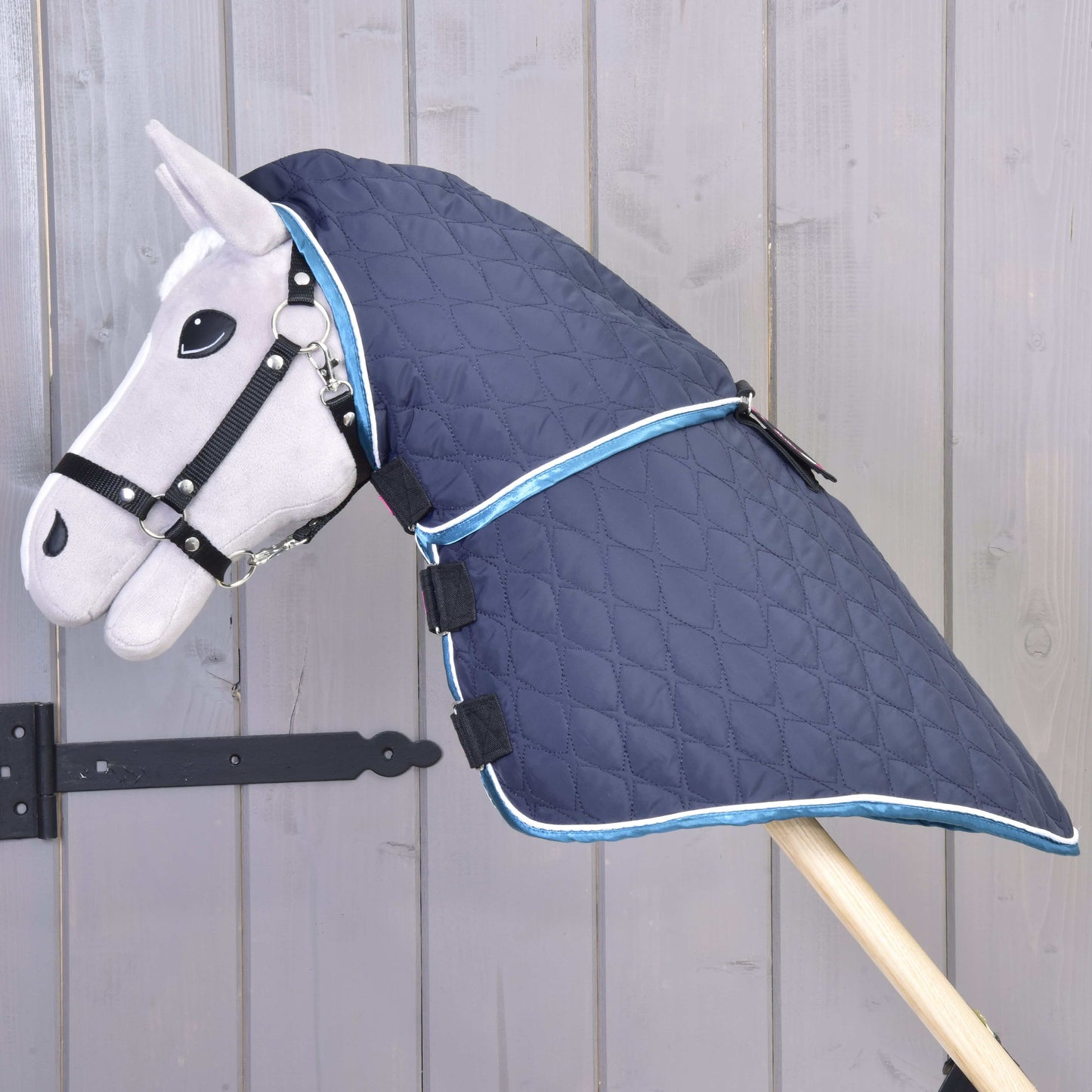 Hobby Horse LarDen Decke mit abnehmbarem Halsteil Mandarin in gestepptem Blau mit hellblauer Einfassung, gezeigt an einem grauen Hobby Horse mit Zaumzeug vor einem Hintergrund aus Holzplanken.