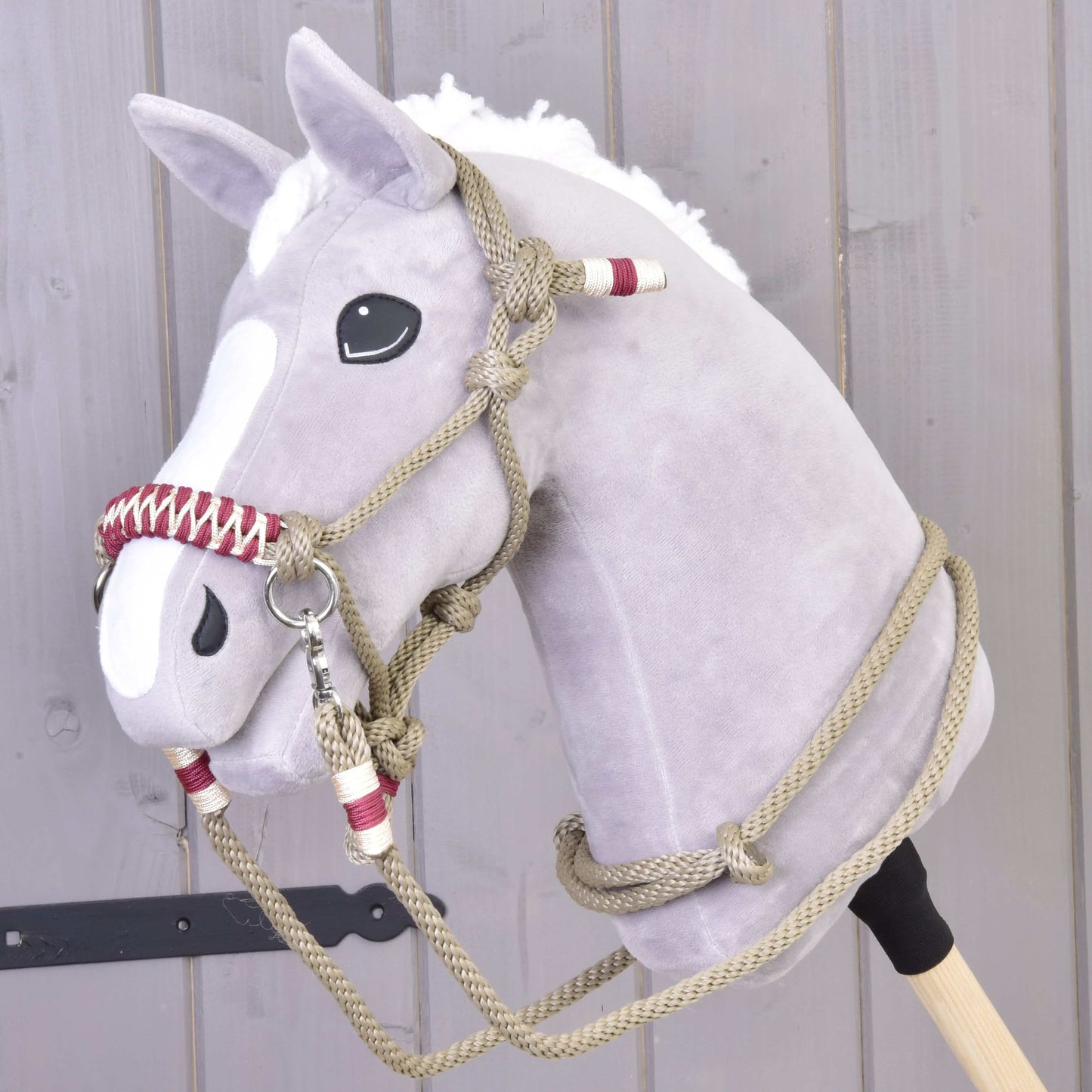 Un Hobby Horse en peluche gris avec crinière blanche et liste blanche, portant l’Ensemble de cordes Élégance de Hobby Horse LarDen, devant un mur en bois clair.