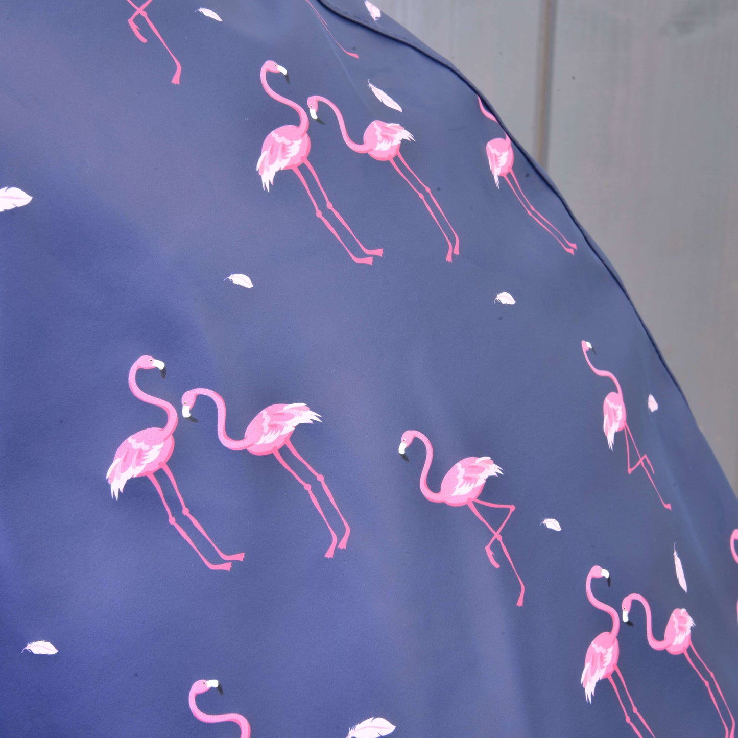 Gros plan sur l’Imperméable Flamant Rose de Hobby Horse LarDen montrant un tissu bleu avec flamants roses et plumes blanches, avec arrière-plan doux et flou, parfait pour les aventures par tous les temps ou les journées de jeu.
