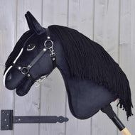 Hobby Horse Freya mit Schwarzem Halfter von Hobby Horse LarDen mit weißer Blesse und schwarzer Garnmähne auf einem Holzstab, vor einer hellgrauen Holzwand – perfekt für jeden Pferdefan in der Familie.