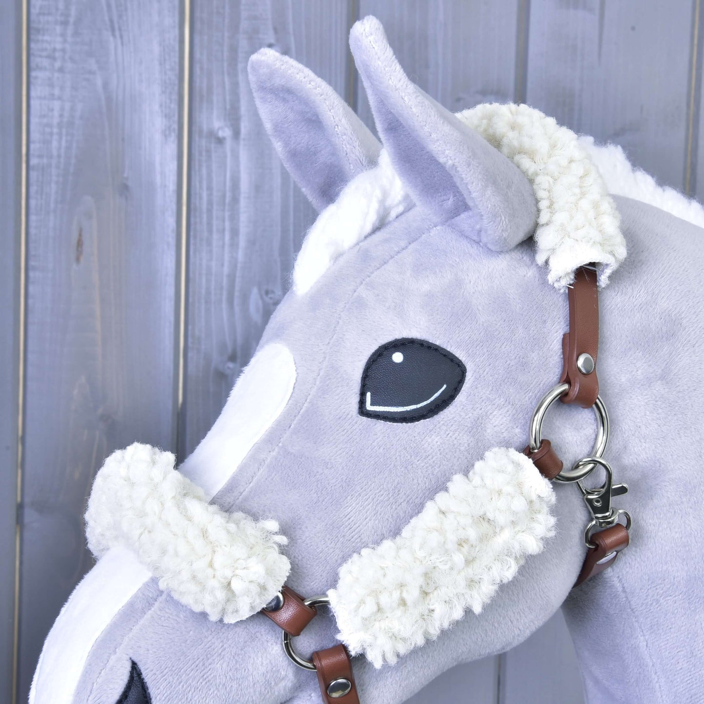 A close-up of a Hobby Horse LarDen toy featuring a brown halter with complete fur-leatherette, gray fleece details, and set against a wooden background.