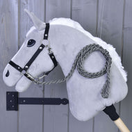 Hobby Horse LarDen „Hobby Horse - Führstrick Knitted Graphite“ mit grauem Plüschkopf, schwarzem Zaumzeug und handgestricktem Führstrick in Graphite auf einem Holzstab, vor einer grauen Holzwand.