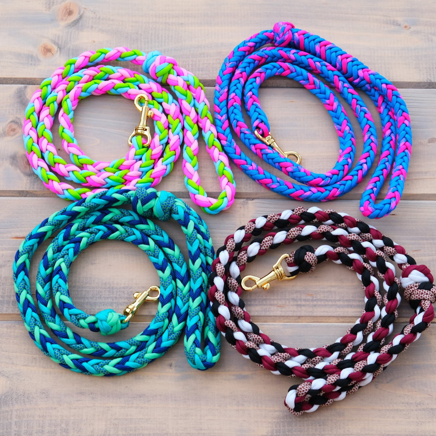Vier farbenfrohe geflochtene Hundeleinen, jeweils mit einem Messingkarabiner, sind ordentlich auf einer Holzoberfläche aufgewickelt – perfekt für Spaziergänge oder auch zur Verwendung als Zügel im Hobby Horsing. Die leuchtenden Farben Neongrün, Pink, Blau, Petrol und Kastanienbraun stechen besonders schön hervor.