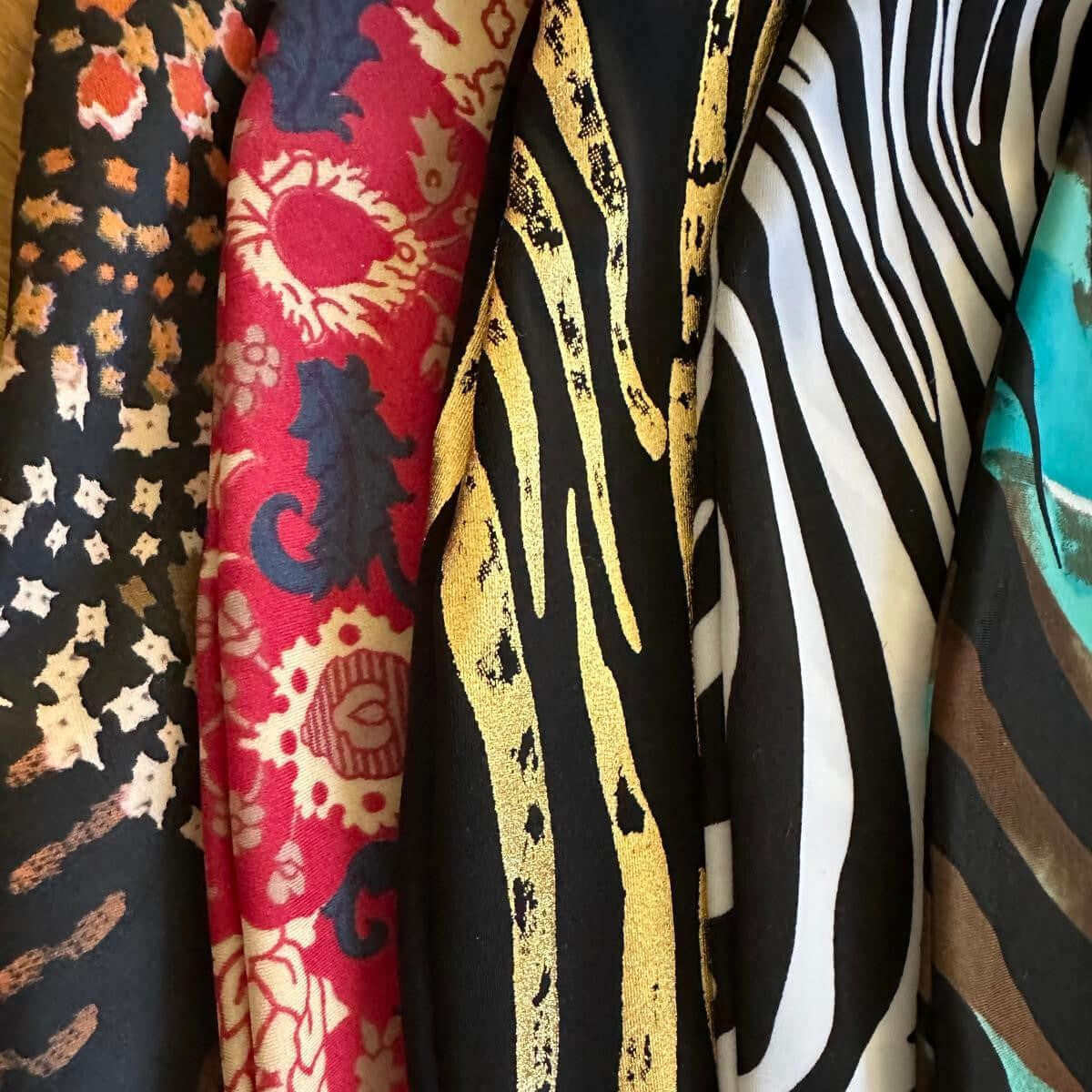 Nahaufnahme von fünf farbenfrohen Stoffen – ideal als Zubehör für Hobby Horse – mit Tiermuster, rotem und cremefarbenem Blumenmuster, gold-schwarzen Tierstreifen, schwarz-weißen Zebrastreifen und Türkis mit braunen Wirbeln.