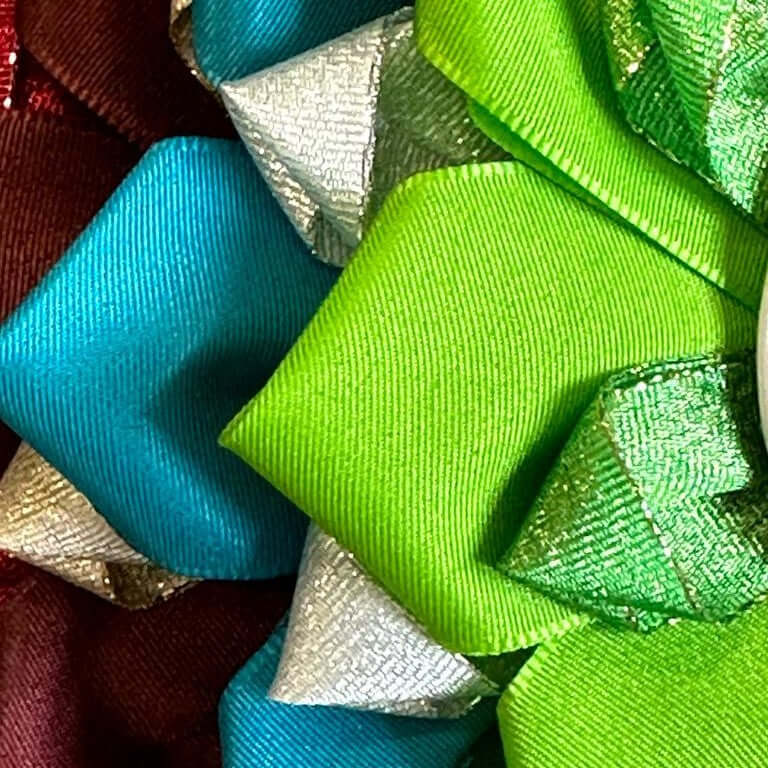 Nahaufnahme von farbenfrohen, mehrlagigen Schleifen in Grün, Blau, Silber und Kastanienrot, perfekt zum Dekorieren eines Hobby Horse oder um dem nächsten Hobby Horsing-Accessoire mit ihrem glänzenden und strukturierten Stoff das gewisse Etwas zu verleihen.