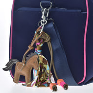 Schlüsselanhänger Horse Brown von Hobby Horse LarDen mit buntem Schal sowie orangefarbenen und rosa Perlen als Accessoire an einer marineblauen Tasche mit rosa Besatz und blauem Gurt, perfekt für Hobby Horsing Fans.