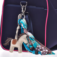 Schlüsselanhänger Horse Grey von Hobby Horse LarDen an einer marineblauen Tasche mit rosa Besatz, mit einem bunt gemusterten Schal, der an einem der Metallringe der Tasche zur Schleife gebunden ist.