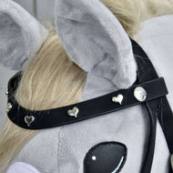 Close-up of a gray plush hobby horse head with the Hobby Horse LarDen Complete De Luxe bridle, featuring two detachable browbands adorned with small silver hearts and round studs. The horse has a light blonde mane and large, soft ears.