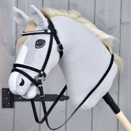 The Hobby Horse LarDen Complete De Luxe bridle with 2 browbands is seen on a realistic gray hobby horse stick toy with a white mane and combined noseband, shown mounted on a wooden stick against a gray wooden background.