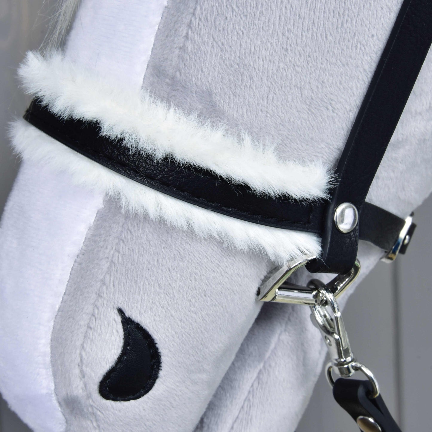 Nahaufnahme von Hobby Horse LarDen Komplette Trense mit Fell: ein weicher, hellgrauer Plüschpferdekopf mit Trense aus Kunstleder, weißem Besatz aus Kunstfell, schwarzem halbmondförmigem Nasenloch-Detail und leicht strukturierter Oberfläche.