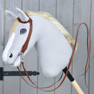 Ein Plüsch-Hobby Horse von Hobby Horse LarDen mit hellgrauem Kopf, weißer Mähne und Komplette Westerntrense Einohr aus Leder mit Split Reins, montiert auf einem Holzstab vor einer grauen Holzwand.