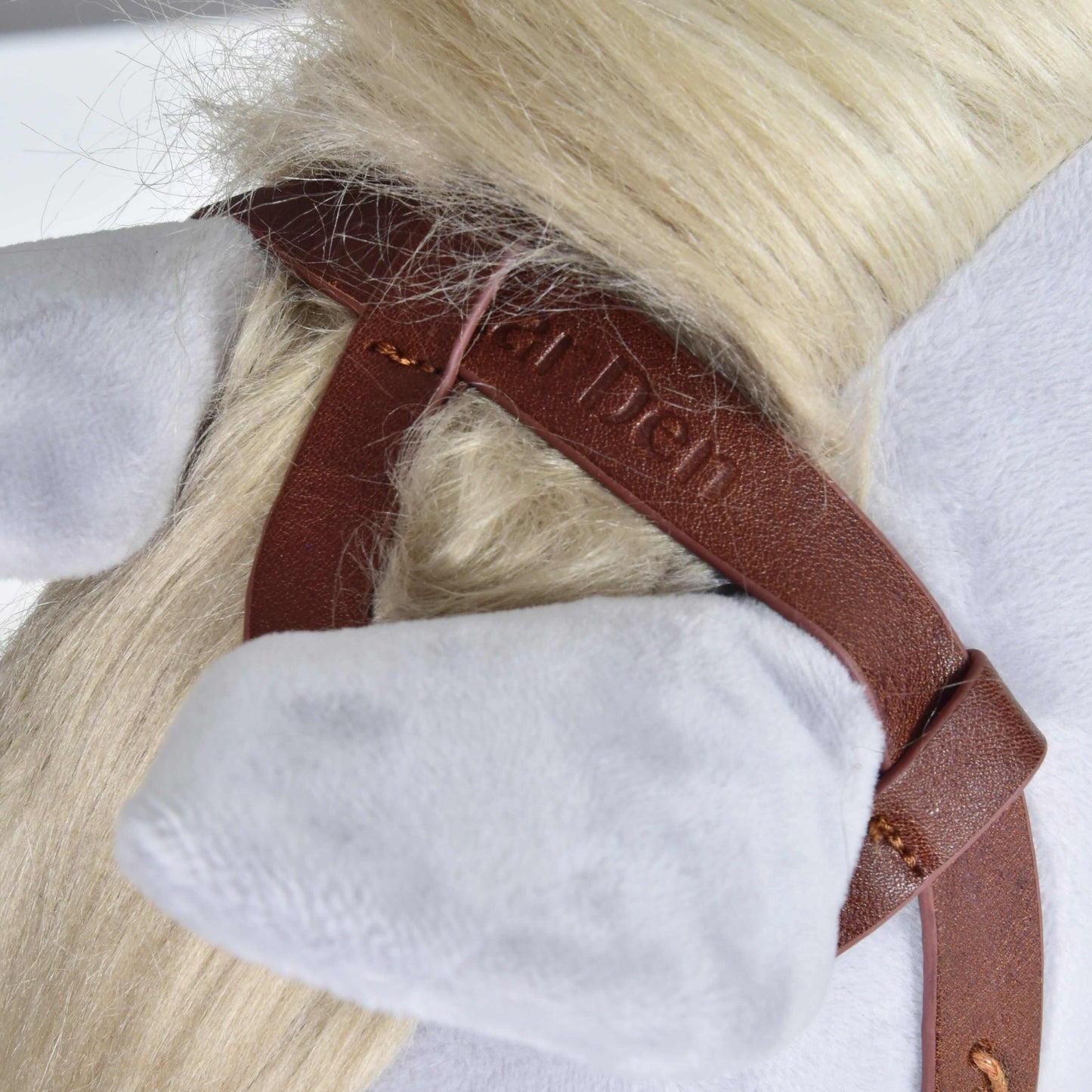 Close-up of a plush horse's head with light gray ears, a cream mane, and a brown Hobby Horse LarDen Complete Western bridle One-Ear featuring stitching, an embossed logo, and split reins.
