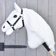Hobby Horse Lady mit Schwarzem Halfter von Hobby Horse LarDen mit weißem Pferdekopf, langer Garnmähne, schwarzem Halfter und markanten schwarzen Augen auf einem Holzstab, vor grauem Holz Hintergrund.