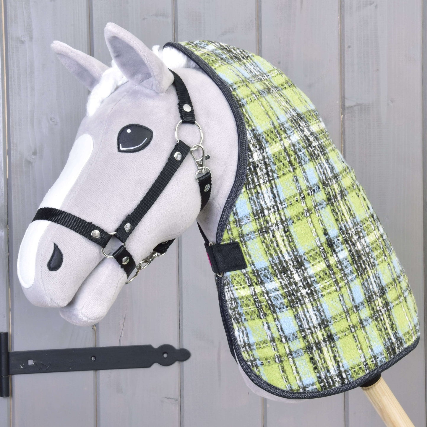 Nahaufnahme eines grauen Steckenpferd-Spielzeugs mit schwarzem Halfter für Hobby Horse und der Stalldecke Lemon Blue von Hobby Horse LarDen vor einem Holzhintergrund.