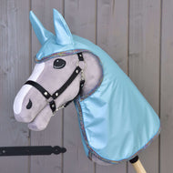 Graues Hobby Horse von Hobby Horse LarDen mit schwarzem Zaumzeug, großen Filzaugen und Regendecke Light Blue mit passendem Ohrenaufsatz, vor einer Holzwand.
