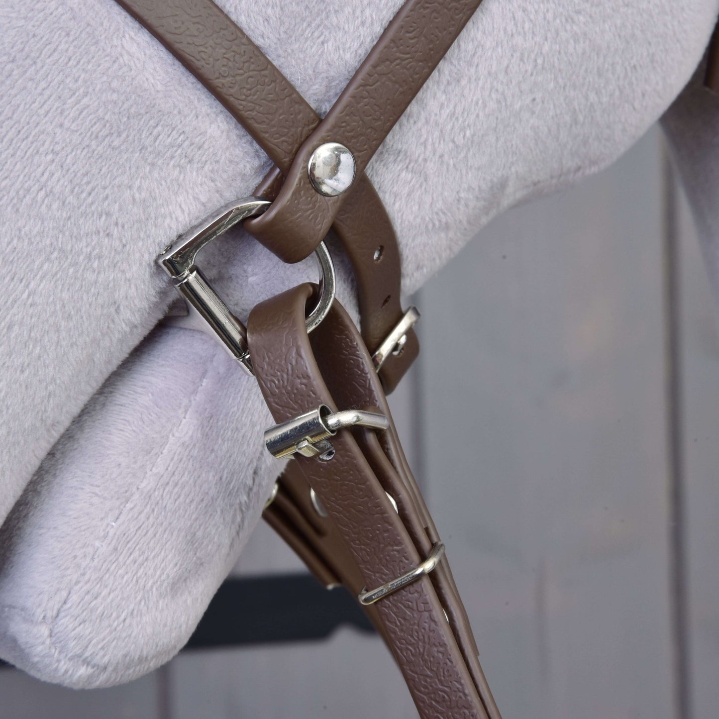 Close-up of the Hobby Horse LarDen Complete bridle with noseband in brown, featuring a metal buckle, attached to a light grey surface with a blurred wooden background.