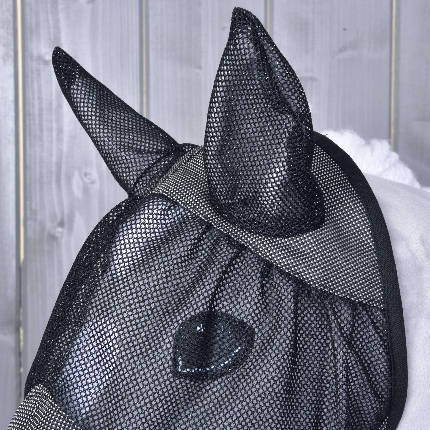 Gros plan d’un cheval portant le Masque anti-mouches De Luxe Gris de Hobby Horse LarDen, avec oreilles couvertes, sur fond en bois gris clair.