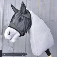 Ein Stoff-Hobby Horse mit hellgrauem Fell trägt die Fliegenmaske de Luxe Grey von Hobby Horse LarDen für zusätzlichen Schutz. Im Hintergrund ist eine Wand aus senkrechten Holzplanken zu sehen.