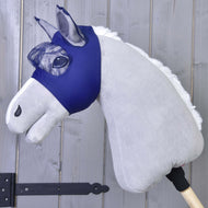 Die Fliegenmaske LarDen von Hobby Horse LarDen zeigt ein Plüsch-Hobby Horse mit hellgrauem Körper, weißer Mähne und waschbarer Fliegenmaske auf einem Holzstock, vor einem Holzpaneel-Hintergrund.