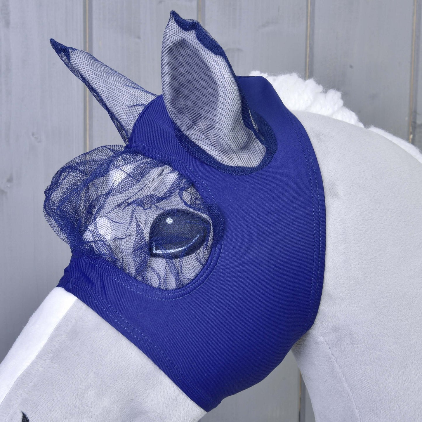 Masque anti-mouches LarDen de Hobby Horse LarDen sur un jouet Hobby Horse en peluche blanc, bleu et lavable, couvrant les oreilles et les yeux pour la protection, présenté sur un fond en bois clair.